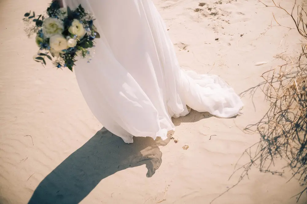 Hochzeits-Fotoshooting in St. Peter-Ording am Strand, in den Dünen. Elegantes Brautkleid weht im Wind.