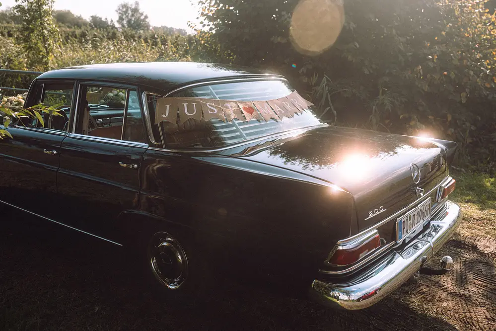 Mercedes-Benz 200 Hochzeitsauto, Oldtimer mit Just-Married-Girlande. Gegenlicht, Lens Flares. Leica M10 M11. Tiffen Black Pro Mist.