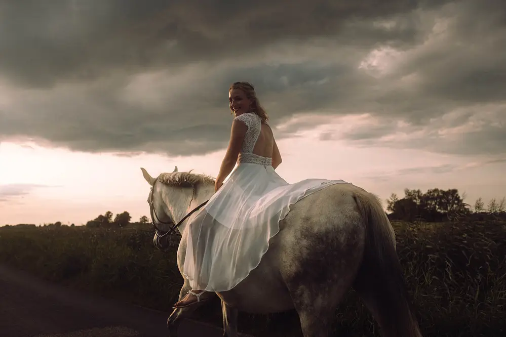 Braut reitet in den Sonnenuntergang. Weißes Brautkleid, weißes Pferd. Hochzeitsfoto.